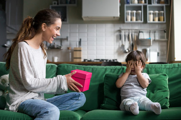 Young smiling mother giving little funny daughter present on her birthday, laughing single mum...