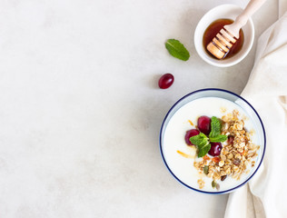Healthy breakfast with bowl of homemade granola with yogurt, fresh cranberries, honey and mint. Vegetarian food concept. Top view. Copy space.