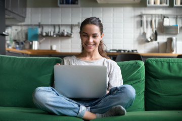 Happy smiling woman sitting on sofa, couch and using laptop at living room at home, watching funny...