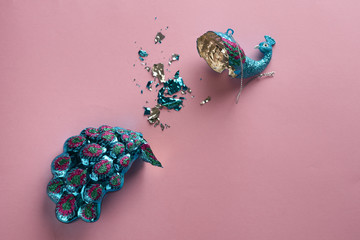 Broken Christmas Toy. Crashed bauble. Damages Gorgeous glass peacock on pink background.