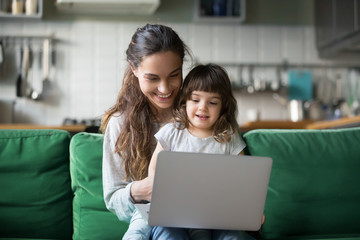 Happy laughing single mother and little preschool cute daughter using laptop online application,...