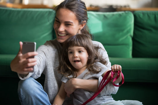 Happy smiling single mother making selfie, mum posing with small preschool cute daughter on cell mobile phone, young mum taking photo with little girl at home, family having fun together
