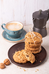 Cup of coffee, oatmeal cookies, coffee maker on white wooden background. Bright morning