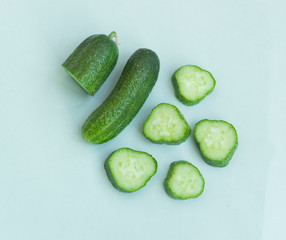 Fresh and sliced cucumbers on light blue background