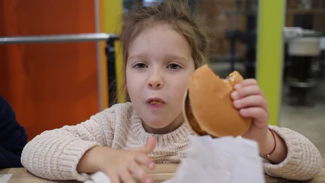 Child girl eating portrait does not like a burger in fast food restaurant spit it out on a table