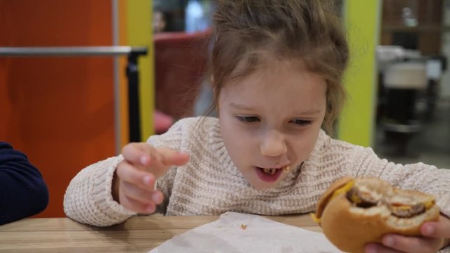 Child girl eating portrait does not like a burger in fast food restaurant spit it out on a table