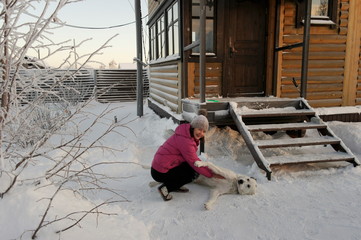 woman in bright jacket playing with big white dog in the snow