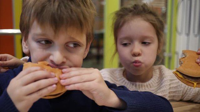 Hungry children greedily eating burgers boy and girl sit in fast food restaurant