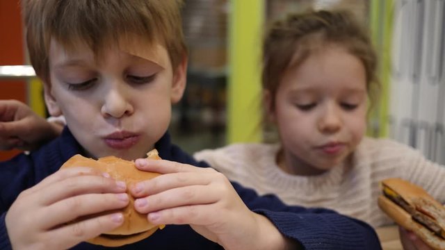 Hungry children greedily eating burgers boy and girl sit in fast food restaurant