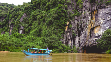 Naklejka premium A cave entrance and a boat seen from the river bank in Phong Nha Khe Bang, Vietnam