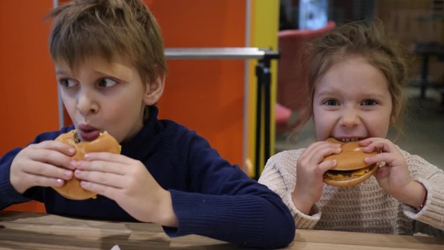 Hungry children funny eating burgers boy and girl sit in fast food restaurant