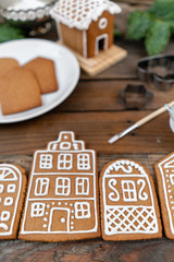 A lot of ginger biscuits in the form of European houses on brown wooden table. Decorated with white sweet glaze. Christmas mood, winter morning.