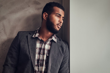 African-American guy leaning on a wall and looking away.
