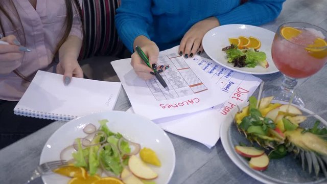 slimming female with diet planning calendar do count calories on sheet of paper during healthy food time in restaurant close-up