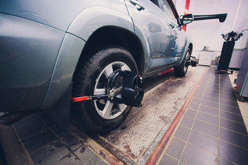 Mechanic tuning aligner for wheel alignment in garage closeup. Professional car maintenance in modern workshop.