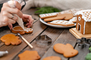 A young girl decorates ginger cookies in the form of snowman Christmas winter morning. Woman draws Icing on honey gingerbread cookies. Wooden brown table. copy space.