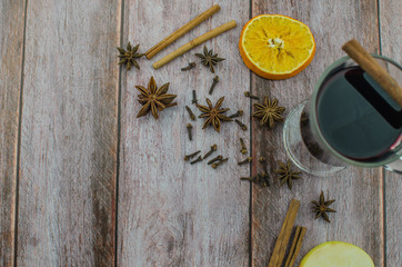 Hot mulled wine drink with lemon, apple, cinnamon, anise and other spices in a glass cup between fir tree branches on wooden cutting board