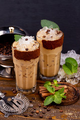 Two glasses of iced latte coffee with ice cubes and milk at decorated with mint and coffee beans wooden table background.