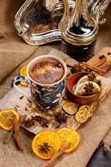 Closeup cup of turkish spiced coffee at decorated wooden table with orange chips, cennamon sticks and sack clothing background.