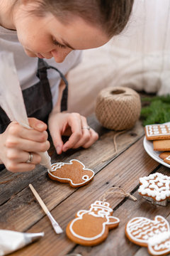 cookies in the form of mittens. A young girl decorates ginger cookies Christmas winter morning. Woman draws Icing on honey gingerbread . Wooden brown table. copy space.