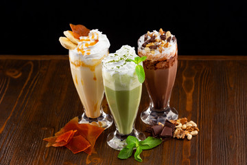 Three glasses with caramel, mint and chocolate cocktails decorated with whipped cream at wooden...