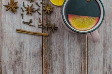 Hot mulled wine drink with lemon, apple, cinnamon, anise and other spices in a glass cup between fir tree branches on wooden cutting board