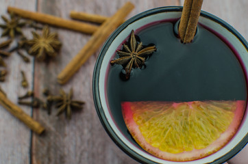 Hot mulled wine drink with lemon, apple, cinnamon, anise and other spices in a glass cup between fir tree branches on wooden cutting board