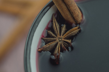 Hot mulled wine drink with lemon, apple, cinnamon, anise and other spices in a glass cup between fir tree branches on wooden cutting board