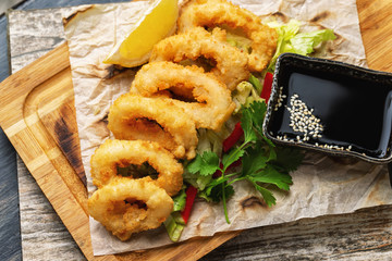 Top view image of golden crispy dried calamari rings with soy sauce served on paper at wooden table background.