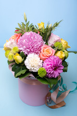 beautiful floral arrangement in the box, pink and yellow rose, pink eustoma, green and pink chrysanthemum, white carnation, pink dahlia on a blue, turquoise background with space for text