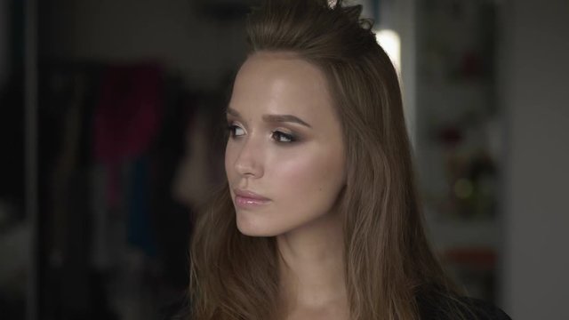 Young beautiful brunette woman with brown eyes demonstrates professional trendy makeup in beauty room on natural light, turns her face, looking into camera. Close up shot.