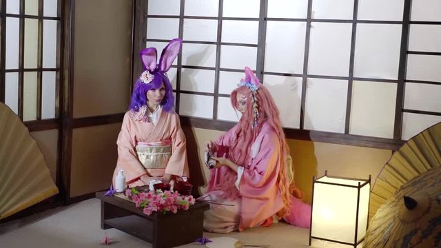 artistic shot of two unusual geishas, sitting on floor in room, one of them is unwrapping parchment scroll