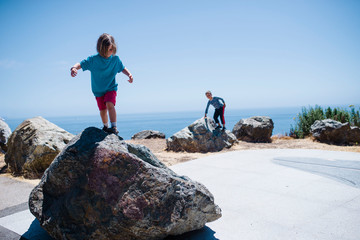 Siblings playing on rocks against sea and sky during sunny day