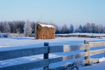 winter landsgape with original haystack and old wooden fence in deep snow and hoarfrost