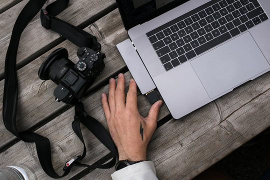 Millennial freelance photographer or social media influencer and content creator. Inserts memory card from camera into work laptop, for editing and photo correction. Creative process and workflow