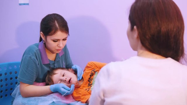 Medicine clinic. A baby with cerebral palsy disease. Speech therapy massage, a woman works with special instrument in the mouth