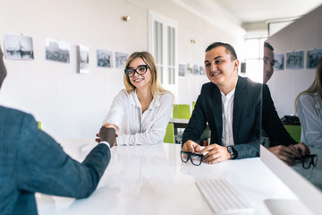 Welcome on board. Handsome afro american man shaking hands with handsome woman smile while sitting on the couch at office with their coworkers