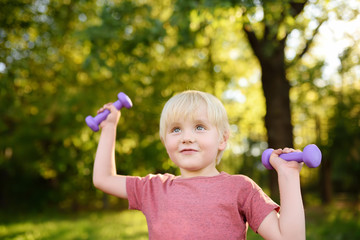 Cute little boy lifting dumbbells outdoors