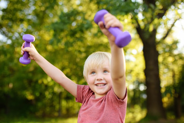 Cute little boy lifting dumbbells outdoors