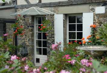 Fototapeta na wymiar Ville d'Agon-Coutainville, volets blancs et porte entourés de fleurs mauves et oranges, département de la Manche, France