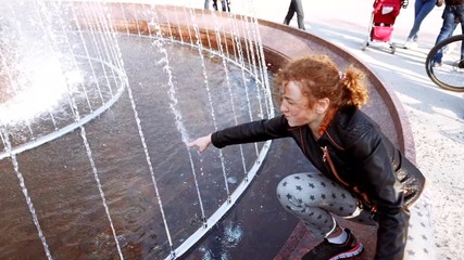 Cute girl walking outdoors and touching water stream from old stone fountain in park. Gush of water drops. splash of dripping water. Child having fun near fountain with flowing water.