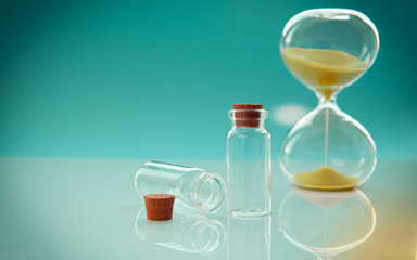 Empty little bottles with cork stopper and hourglass on toned background, close-up