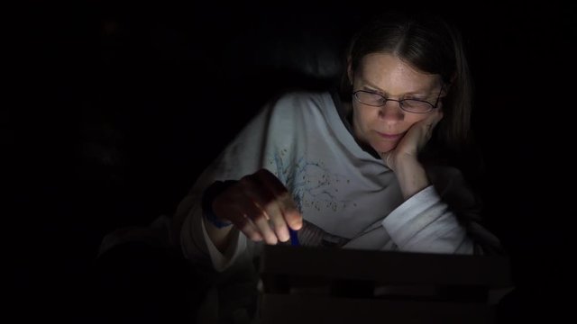 Woman searching scrolling and shopping on iPad tablet in the dark late at night.