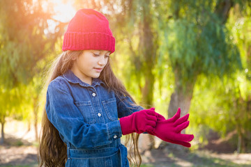 Cute Mixed Race Young Girl Wearing Red Knit Cap Putting On Mittens Outdoors