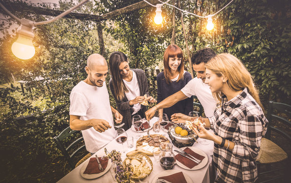 Happy friends having fun eating local food at garden fest - Friendship and holidays concept with people together at farmhouse vineyard winery - Warm vintage filter with artificial electric lighting