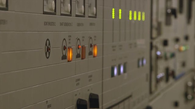 Close up dolly shot of ship engine control room  with dark-cream wall colour,  horizontal lines, orange, red led lights, push switch buttons, green vertical  indicator bars, monitoring instrume