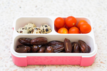 Lunch box filled with dates, tomatoes cherry and quail eggs