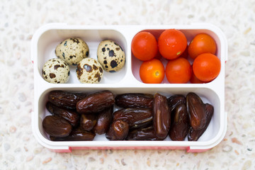 Lunch box filled with dates, tomatoes cherry and quail eggs