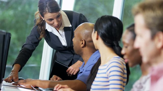 Class mature multi ethnic people on IT business course working with Caucasian American female tutor in classroom 