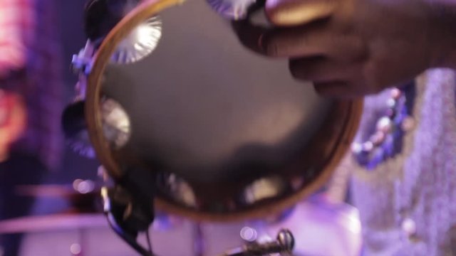 Close up of a artist playing tambourine during a brazilian music festival, with some culture from brazil on a colorful stage